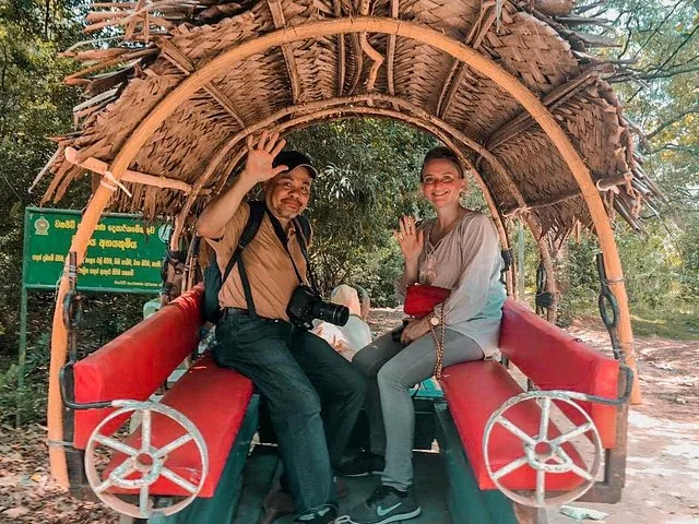 tourists wave from a traditional bullock cart on a dirt road