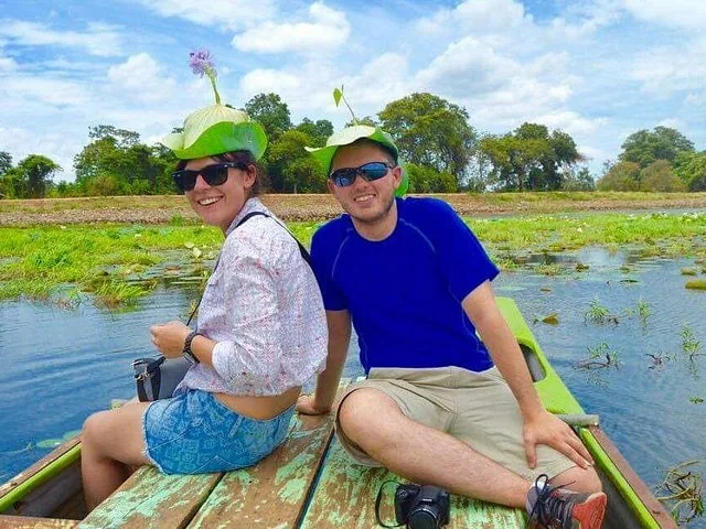 una pareja se sienta en un bote usando sombreros de hojas de loto en un lago